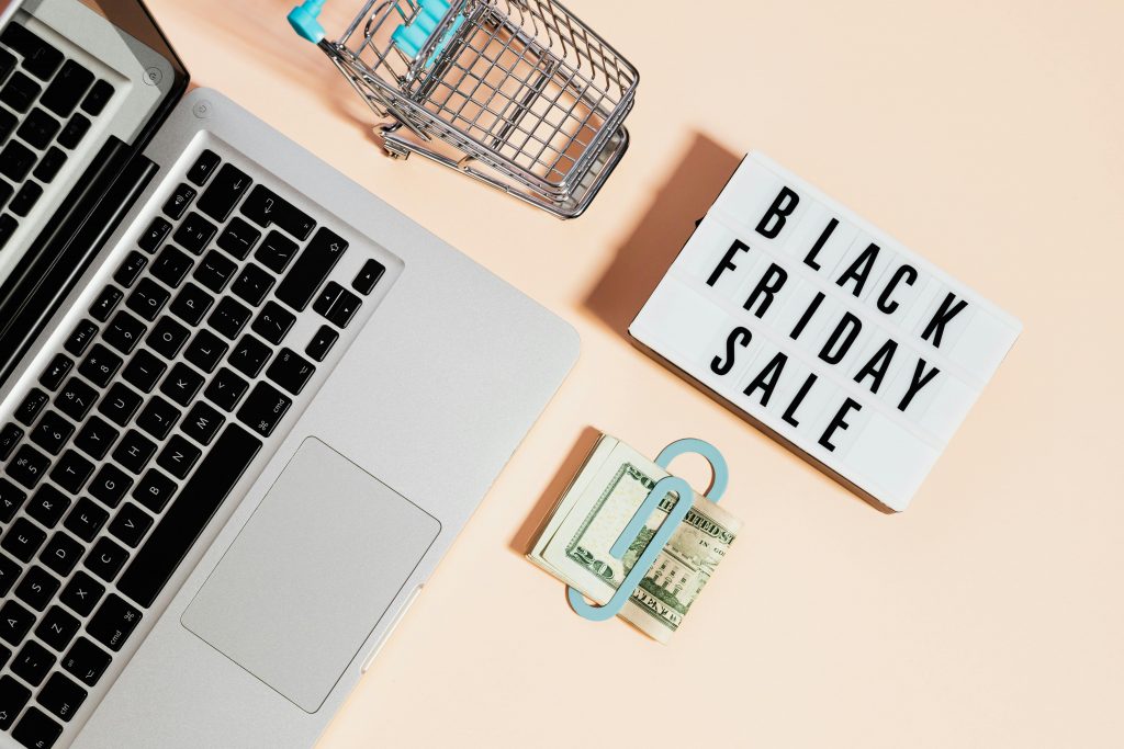 black friday sale sign next to a miniature shopping cart, laptop, and a bundle of cash