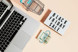 black friday sale sign next to a miniature shopping cart, laptop, and a bundle of cash