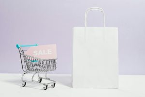'sale' tag in a miniature shopping cart, next to a white shopping bag
